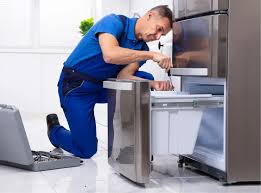 Technician repairing a stainless steel refrigerator with a laptop for diagnostics